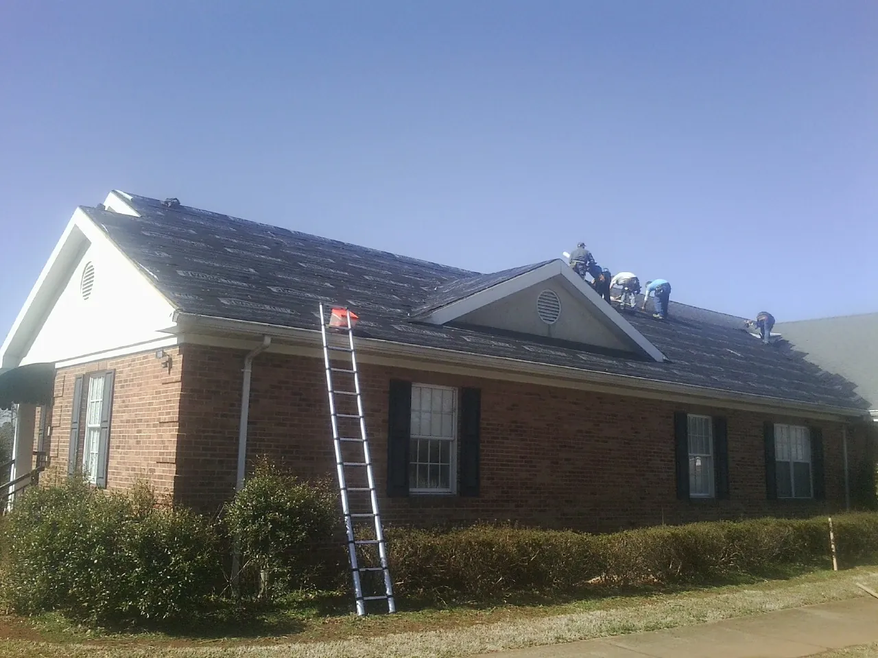 Crew tearing shingles off a brick ranch roof with a ladder set — Metal Roof Repair work by our crew in Homeworth