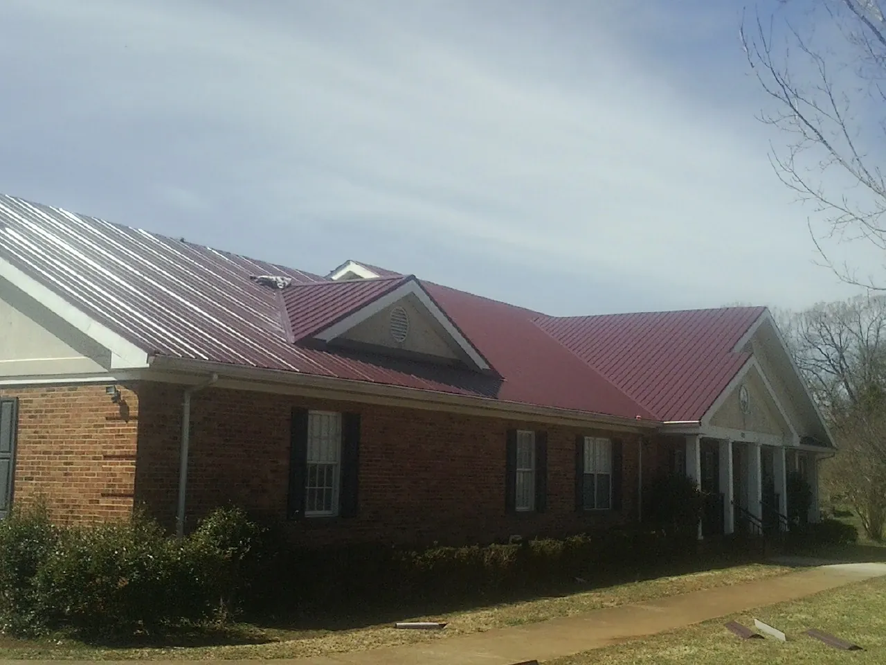 Red metal roof with gabled entries on a long brick building, from a Hail Damage Roof Repair job in Homeworth