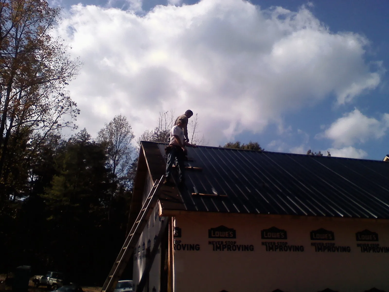 Roofer fastening dark metal panels high against a cloudy sky, from a Roof Inspection job in Homeworth