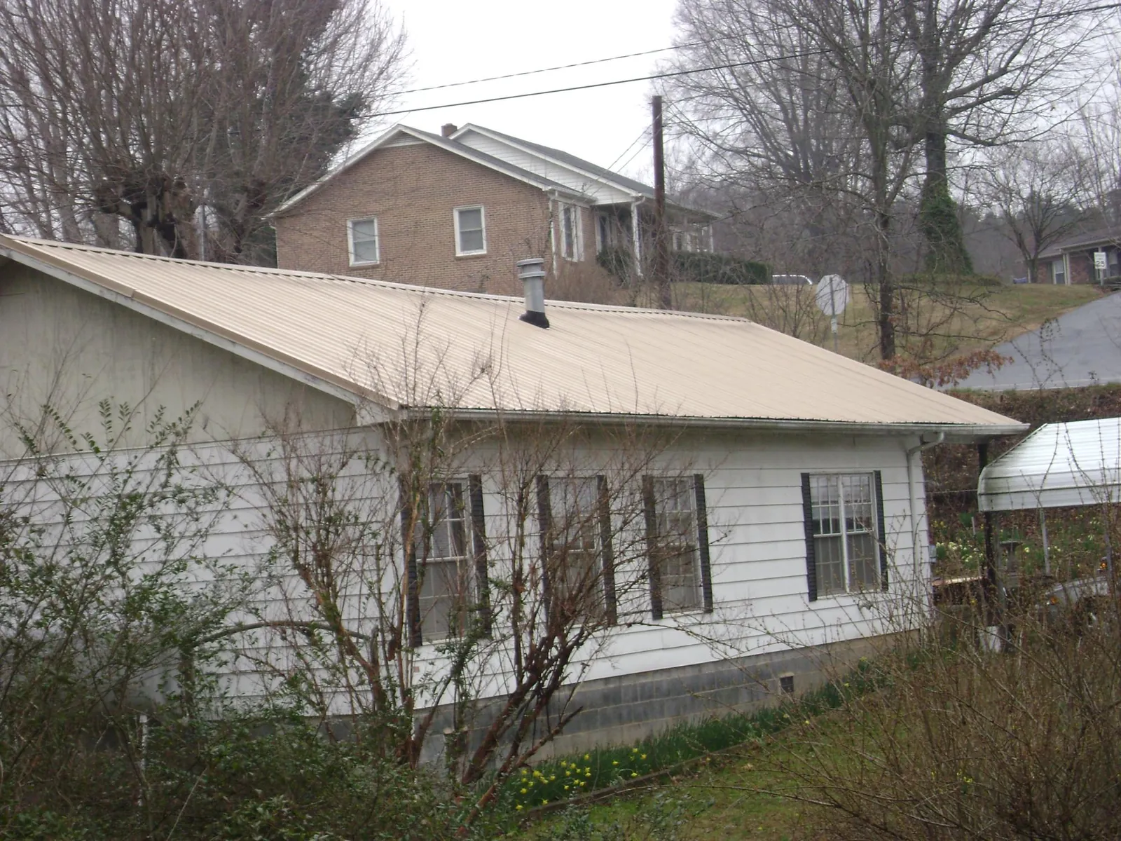 Tan metal roof on a white sided house set into a hillside — Commercial Roofing by Roofing Brothers in Homeworth